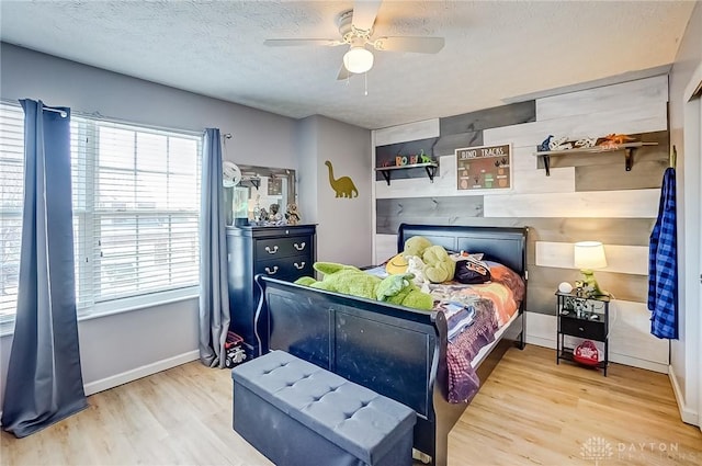 bedroom featuring ceiling fan, wood walls, light hardwood / wood-style flooring, and a textured ceiling