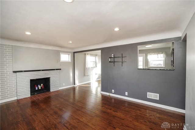 unfurnished living room featuring a brick fireplace and dark hardwood / wood-style floors