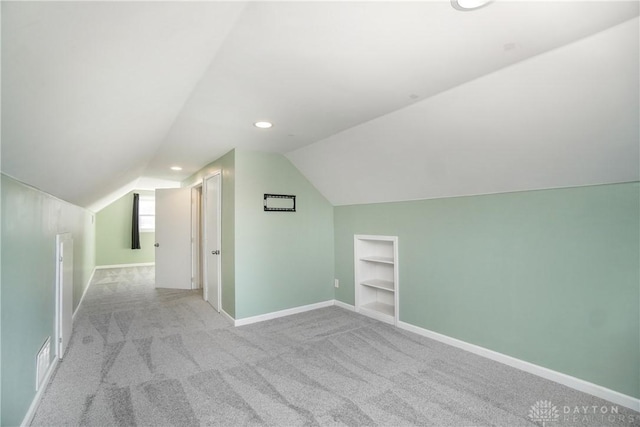 bonus room featuring built in shelves, light colored carpet, and vaulted ceiling