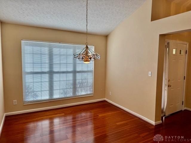 unfurnished dining area with dark hardwood / wood-style flooring, a notable chandelier, and a textured ceiling