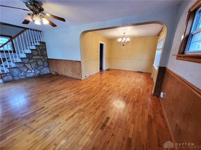 unfurnished living room with ceiling fan with notable chandelier, light hardwood / wood-style flooring, and wood walls