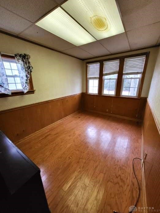 spare room with a drop ceiling, wood-type flooring, and wood walls