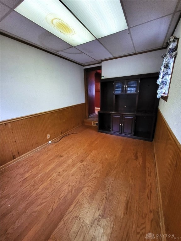 unfurnished living room featuring hardwood / wood-style flooring, wood walls, and a drop ceiling