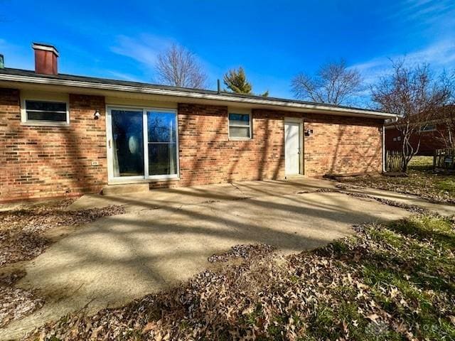 back of house featuring brick siding, a patio, and a chimney