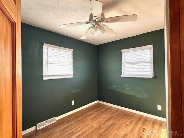 spare room with plenty of natural light, wood finished floors, visible vents, and baseboards