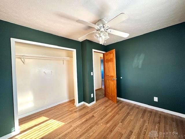 unfurnished bedroom with a closet, ceiling fan, baseboards, and wood finished floors