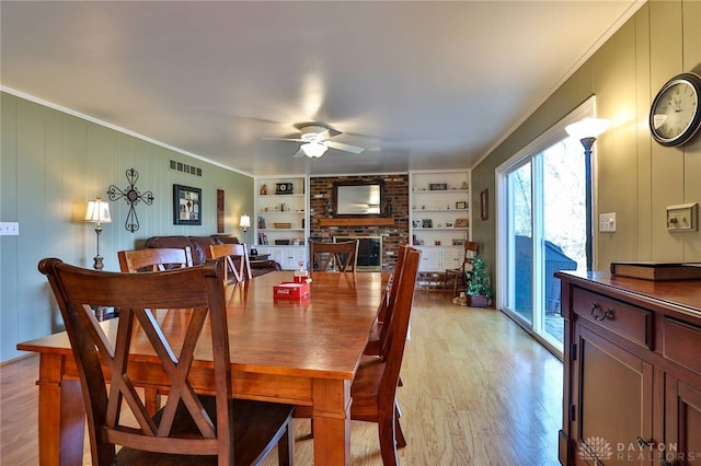 dining space featuring ornamental molding, ceiling fan, a fireplace, and light hardwood / wood-style floors