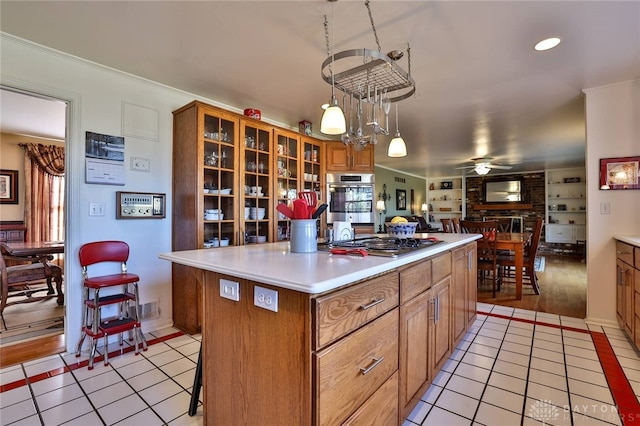 kitchen featuring pendant lighting, light tile patterned floors, stainless steel gas cooktop, a kitchen island, and ceiling fan with notable chandelier