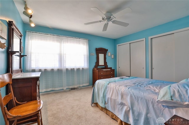 carpeted bedroom with ceiling fan and multiple closets