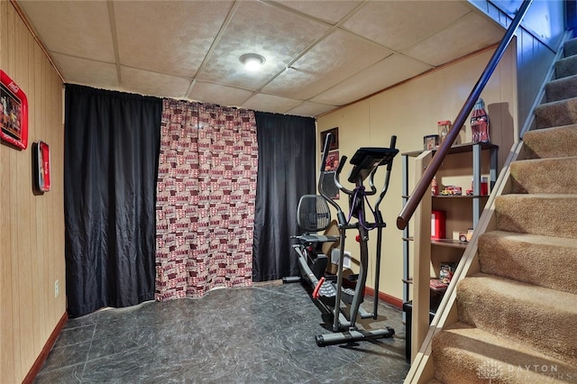 workout room with a paneled ceiling and wood walls