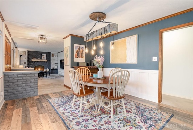 dining space with hardwood / wood-style floors, ornamental molding, and a brick fireplace