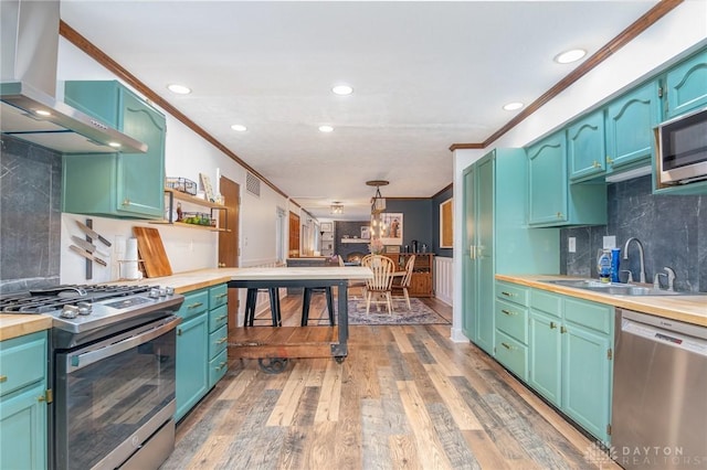 kitchen featuring wall chimney exhaust hood, sink, crown molding, appliances with stainless steel finishes, and hardwood / wood-style flooring