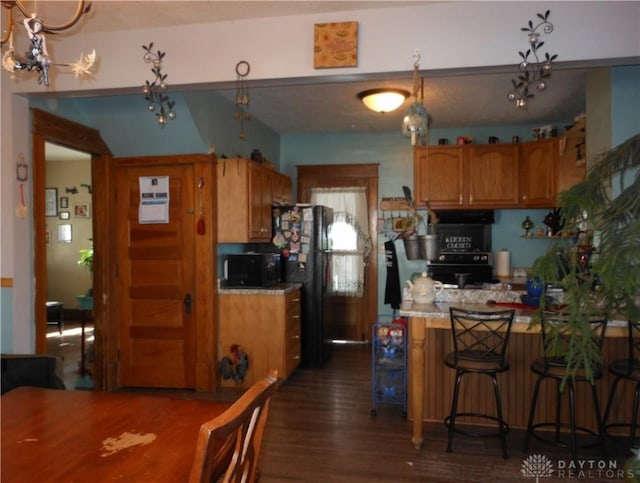 kitchen with dark hardwood / wood-style flooring, black appliances, kitchen peninsula, and a kitchen bar