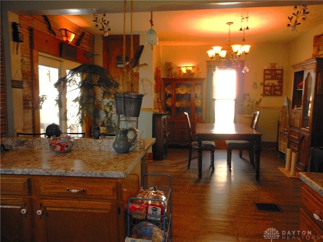 kitchen featuring dark wood-type flooring, decorative light fixtures, light stone countertops, and a notable chandelier