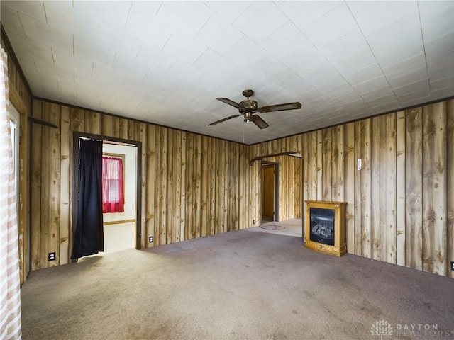 unfurnished living room featuring carpet floors, ceiling fan, and wood walls