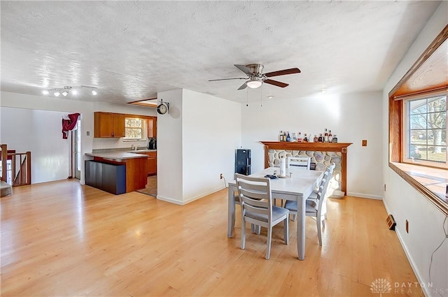 dining area with a textured ceiling, baseboards, light wood-style flooring, and a ceiling fan