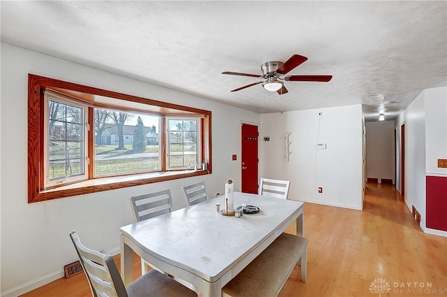 dining room with a ceiling fan, light wood-type flooring, a textured ceiling, and baseboards