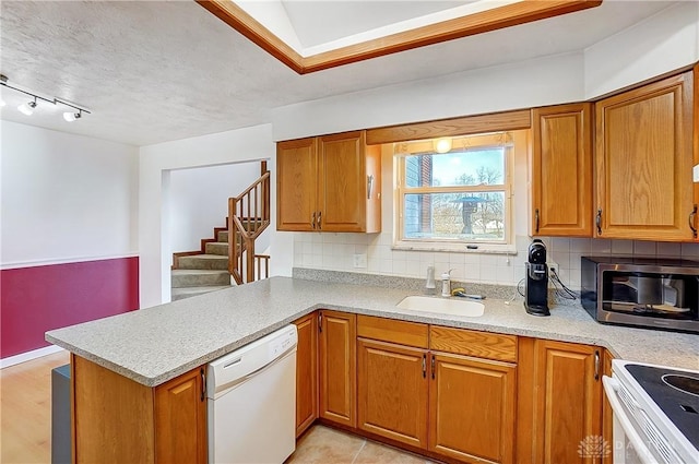 kitchen featuring a peninsula, white appliances, a sink, backsplash, and brown cabinets