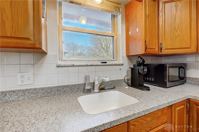 kitchen with tasteful backsplash, light stone counters, brown cabinets, and a sink