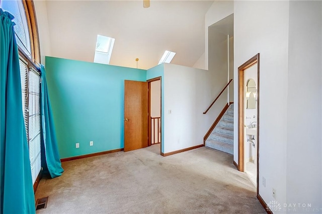 unfurnished room with high vaulted ceiling, light carpet, a skylight, baseboards, and stairs