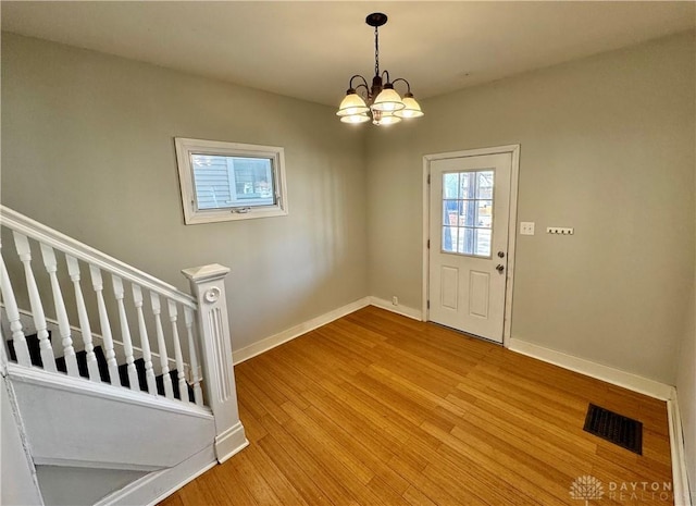 foyer entrance with visible vents, baseboards, stairway, light wood-type flooring, and an inviting chandelier