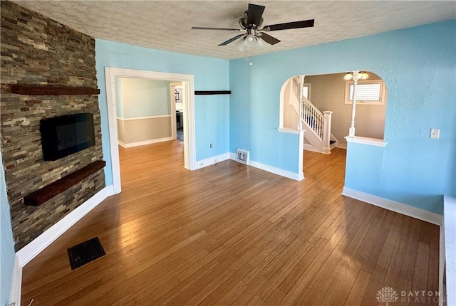 unfurnished living room with hardwood / wood-style flooring, ceiling fan, a stone fireplace, and a textured ceiling