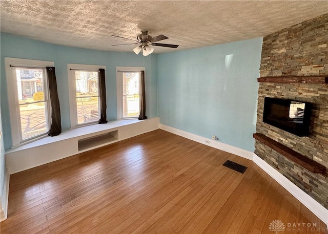 unfurnished living room with a textured ceiling, wood-type flooring, a stone fireplace, and a healthy amount of sunlight