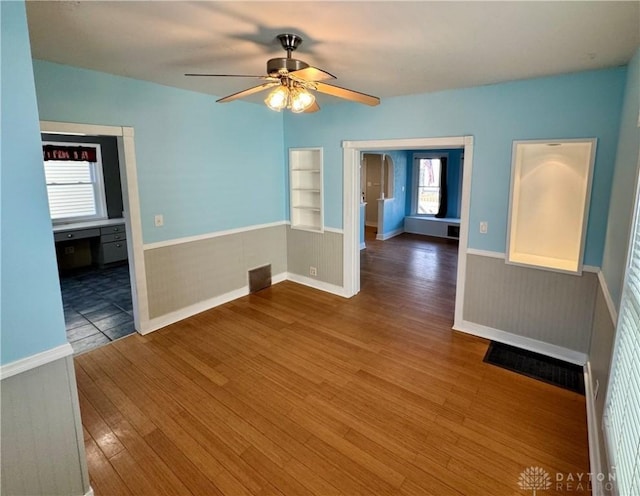 spare room with built in shelves, ceiling fan, and wood-type flooring