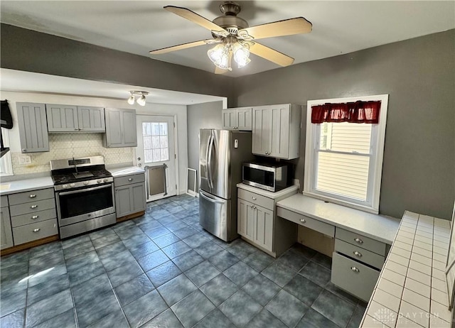 kitchen with backsplash, stainless steel appliances, built in desk, and gray cabinetry