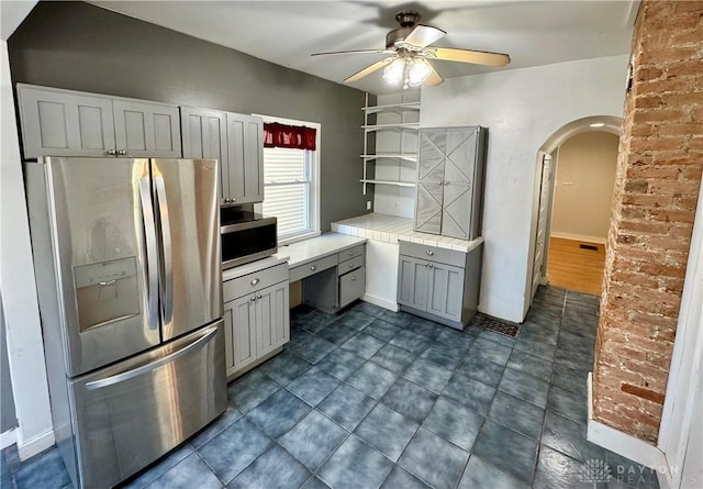 kitchen with appliances with stainless steel finishes, gray cabinetry, dark tile patterned floors, tile counters, and ceiling fan