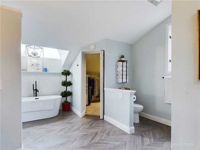 bathroom featuring lofted ceiling with skylight, parquet floors, a bathtub, and toilet