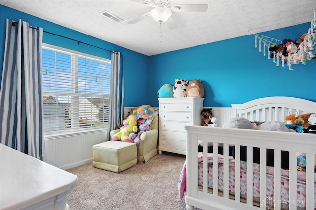 carpeted bedroom with ceiling fan, a crib, and a textured ceiling