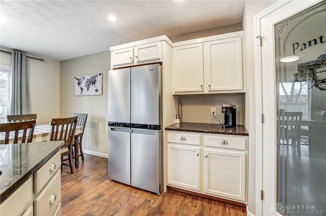 kitchen featuring white cabinetry, hardwood / wood-style floors, stainless steel fridge, and dark stone countertops