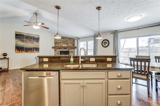 kitchen with dark stone countertops, sink, a stone fireplace, and stainless steel dishwasher