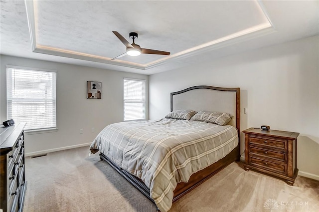 bedroom with ceiling fan, a raised ceiling, and light carpet