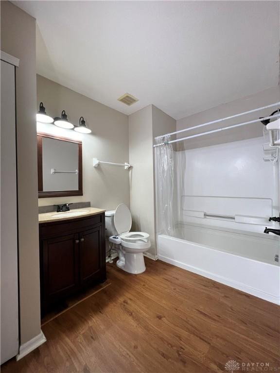 full bathroom with hardwood / wood-style flooring, vanity, shower / tub combo, and toilet