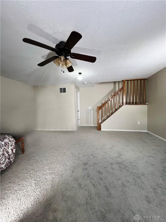 unfurnished living room featuring ceiling fan, carpet, and a textured ceiling