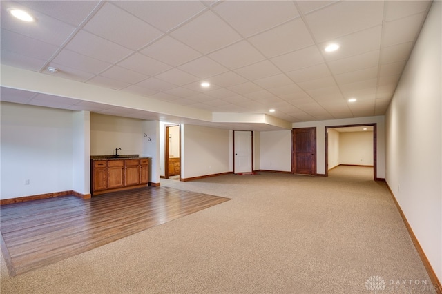 basement featuring a drop ceiling, sink, and light colored carpet