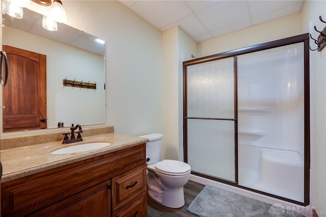 bathroom with hardwood / wood-style floors, vanity, a drop ceiling, toilet, and walk in shower