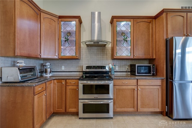 kitchen with dark stone countertops, stainless steel appliances, decorative backsplash, and wall chimney range hood