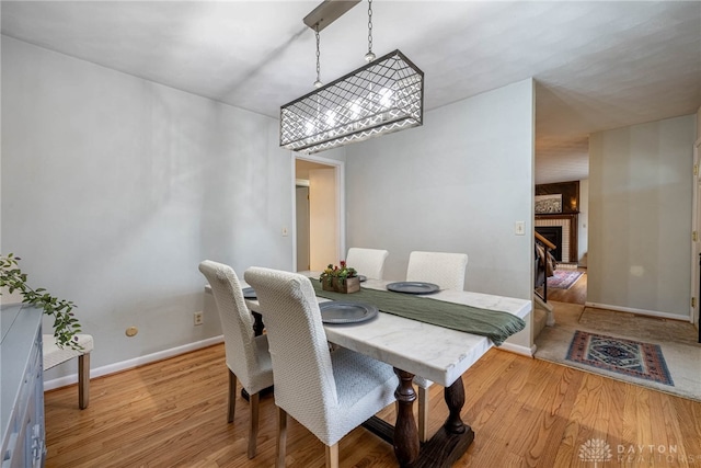 dining area with a brick fireplace, a notable chandelier, and light wood-type flooring