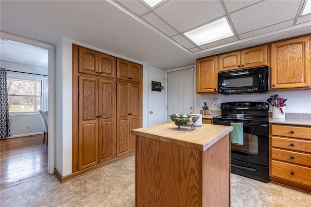 kitchen with butcher block countertops, a paneled ceiling, black appliances, and a center island