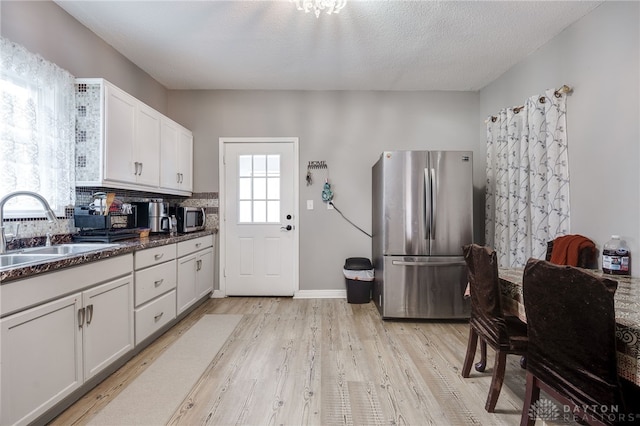 kitchen featuring dark countertops, light wood-type flooring, appliances with stainless steel finishes, white cabinetry, and a sink