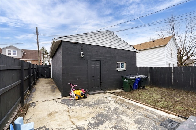 rear view of property featuring concrete block siding, a fenced backyard, and an outdoor structure