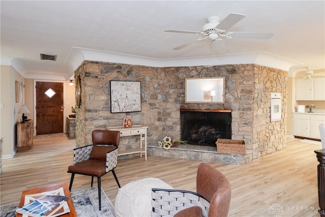 living room featuring a fireplace, ceiling fan, and light wood-type flooring