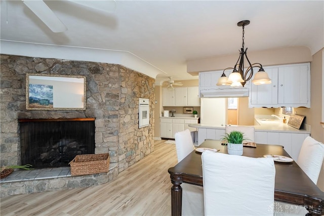 dining area featuring lofted ceiling, a stone fireplace, sink, ceiling fan, and light hardwood / wood-style floors