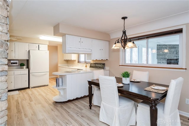 kitchen featuring decorative light fixtures, kitchen peninsula, white fridge, and white cabinets