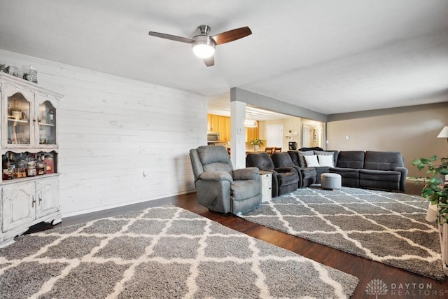 living room featuring dark hardwood / wood-style flooring, wooden walls, and ceiling fan