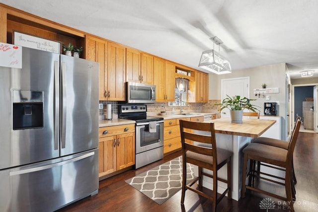 kitchen with appliances with stainless steel finishes, pendant lighting, butcher block countertops, sink, and decorative backsplash