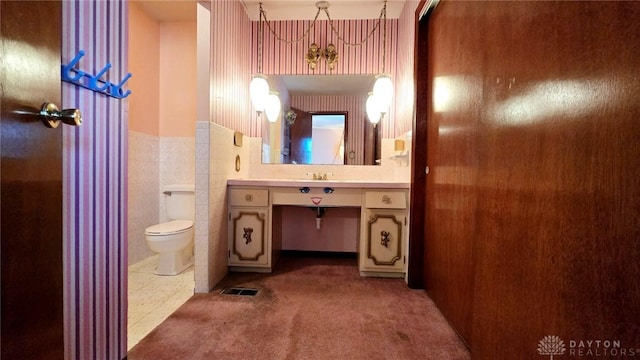 bathroom with tile walls, vanity, a notable chandelier, and toilet